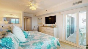 Een slaapkamer met een bed, een plafondventilator, een dressoir, een televisie en een schuifdeur naar een balkon.