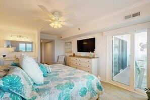 Une chambre à coucher comprenant un lit, un ventilateur de plafond, une commode, un téléviseur et une porte-fenêtre coulissante donnant sur un balcon.