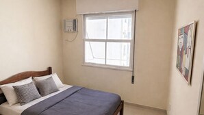 Een slaapkamer met een bed, een raam, een wandairconditioner en een schilderij.