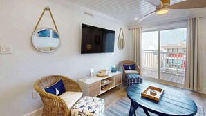 Un salon doté de meubles en osier, d’un téléviseur à écran plat, d’un ventilateur de plafond et d’un balcon offrant une vue agréable.