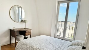 A bedroom with a bed, a desk, a chair, a mirror, and a window with a view. - celine 19  (Paris)