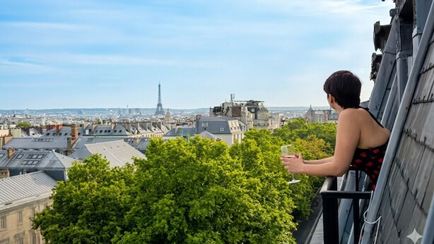 A person on a balcony overlooking a cityscape with buildings and a tower in the distance. - celine 19  (Paris)