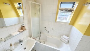 A bathroom with a white sink, a bathtub, a shower, and a window. - celine 19  (Paris)