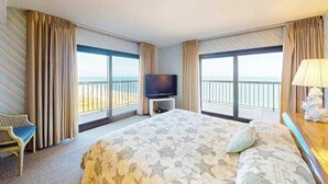 Ein Hotelzimmer mit einem großen Bett, einem Fernseher, einem Sessel und einem Balkon mit Blick.