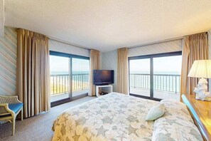 Ein Hotelzimmer mit einem großen Bett, einem Fernseher, einem Sessel und einem Balkon mit Blick.