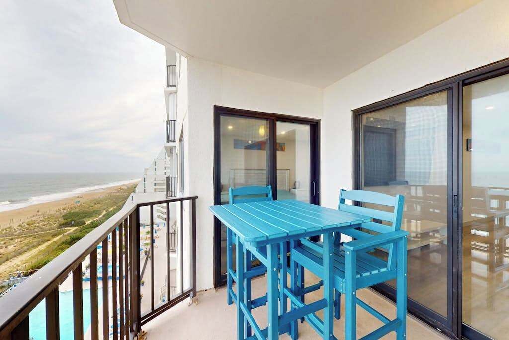A balcony with a table and chairs, a glass door, and a view of the beach.