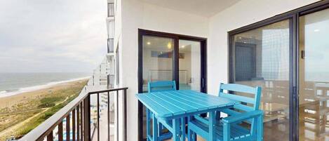 A balcony with a table and chairs, a glass door, and a view of the beach.