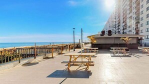 A beachside patio with picnic tables, a railing, and a building with balconies overlooking the ocean. - Plaza 811 (Ocean City)