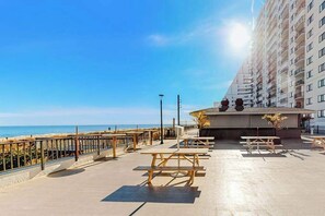 A beachside patio with picnic tables, a railing, and a building with balconies overlooking the ocean. - Plaza 811 (Ocean City)