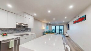 A modern kitchen with a large island, stainless steel appliances, and a view to a balcony. - Plaza 811 (Ocean City)