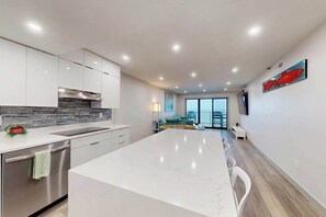 A modern kitchen with a large island, stainless steel appliances, and a view to a balcony. - Plaza 811 (Ocean City)