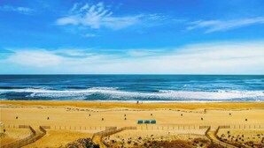 A beach with a clear sky, sandy shore, and a fenced area with structures. - Plaza 811 (Ocean City)