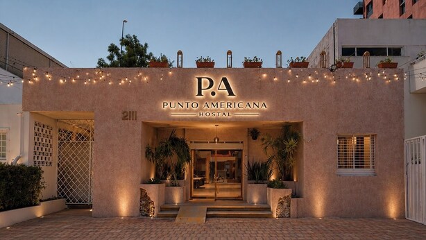 A hotel entrance with a sign reading 'PUNTO AMERICANA HOSTAL' and a paved driveway leading to the entrance. - PUNTO AMERICANA HOSTAL (Guadalajara)