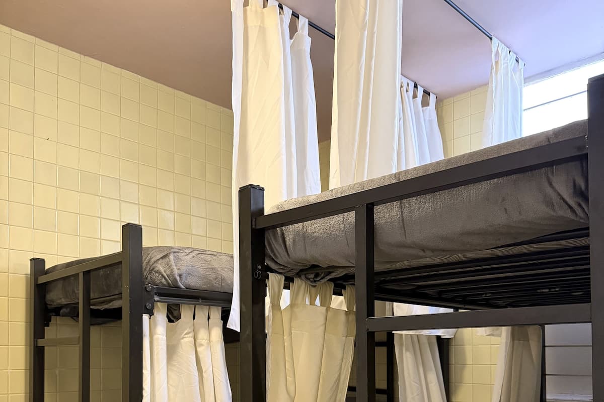 Dormitorio con literas, cortinas blancas, ventilador de techo y alfombra estampada.