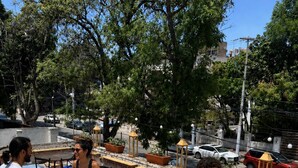 An outdoor seating area with tables and chairs, surrounded by trees and a street view. - PUNTO AMERICANA HOSTAL (Guadalajara)