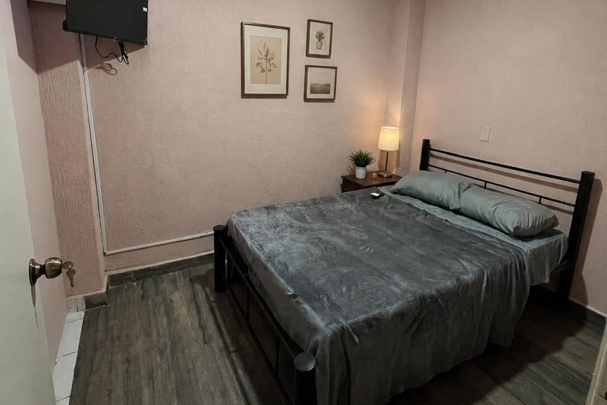 Un dormitorio con una cama, un ventilador de techo, un televisor montado en la pared y cuadros enmarcados.