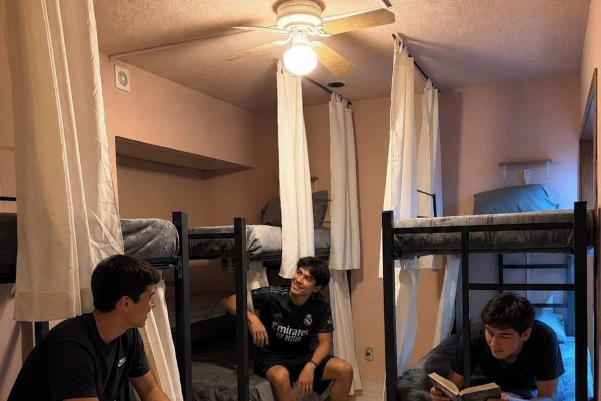 Un dormitorio con literas, un ventilador de techo y una persona leyendo un libro.