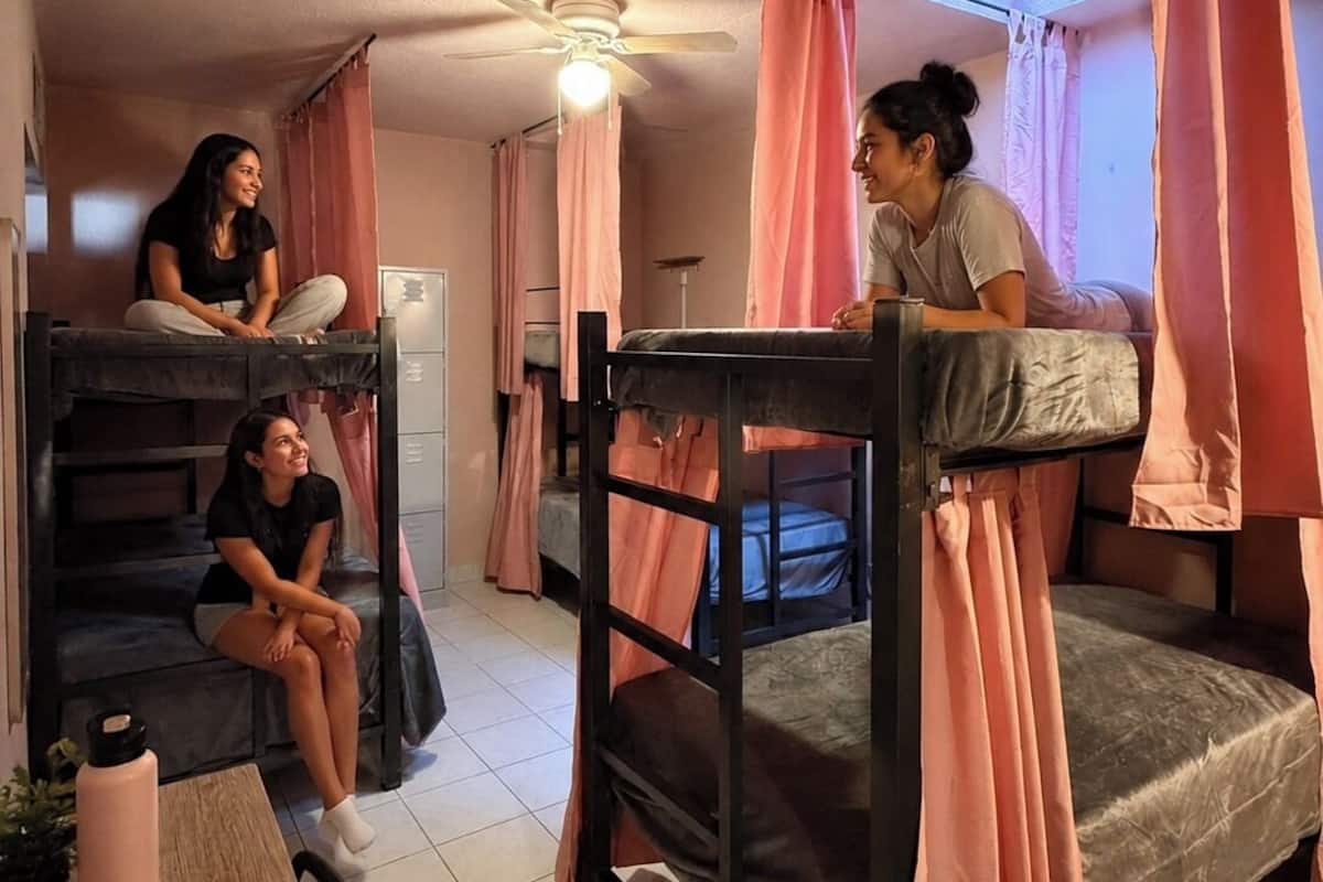 Un dormitorio con literas, ventilador de techo y una pequeña mesa con un libro y una botella de agua.