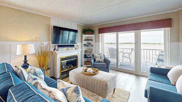 A living room with a TV, sofas, a fireplace, and a balcony with outdoor furniture. - Luxury waterfront condo w/water views from balcony, shared pool, AC & free WiFi (Ocean City)