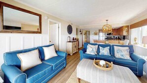 A living room with two blue sofas, a coffee table, and a kitchen in the background. - Luxury waterfront condo w/water views from balcony, shared pool, AC & free WiFi (Ocean City)