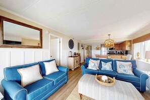 Een woonkamer met twee blauwe banken, een salontafel en een keuken op de achtergrond.