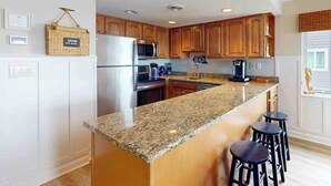 A kitchen with granite countertops, wooden cabinets, a refrigerator, a microwave, and a coffee maker. - Luxury waterfront condo w/water views from balcony, shared pool, AC & free WiFi (Ocean City)