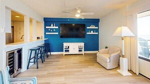 Een moderne woonkamer met een blauwe accentmuur, een flatscreen televisie, een plafondventilator, een bank en een bar met barkrukken.