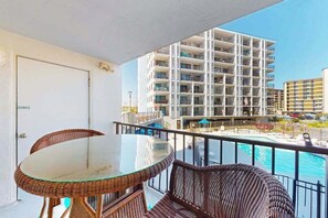 A balcony with wicker furniture, a glass table, and a view of a high-rise building and a pool. - Bluewater East 202S (Ocean City)