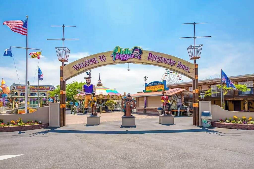Un letrero de bienvenida en la entrada de un parque de atracciones, con un cielo despejado.