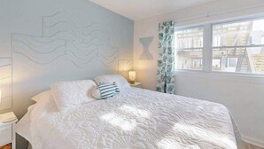 A bedroom with a bed, nightstands, a wall art piece, and a window with curtains. - Robin View 2 (Ocean City)