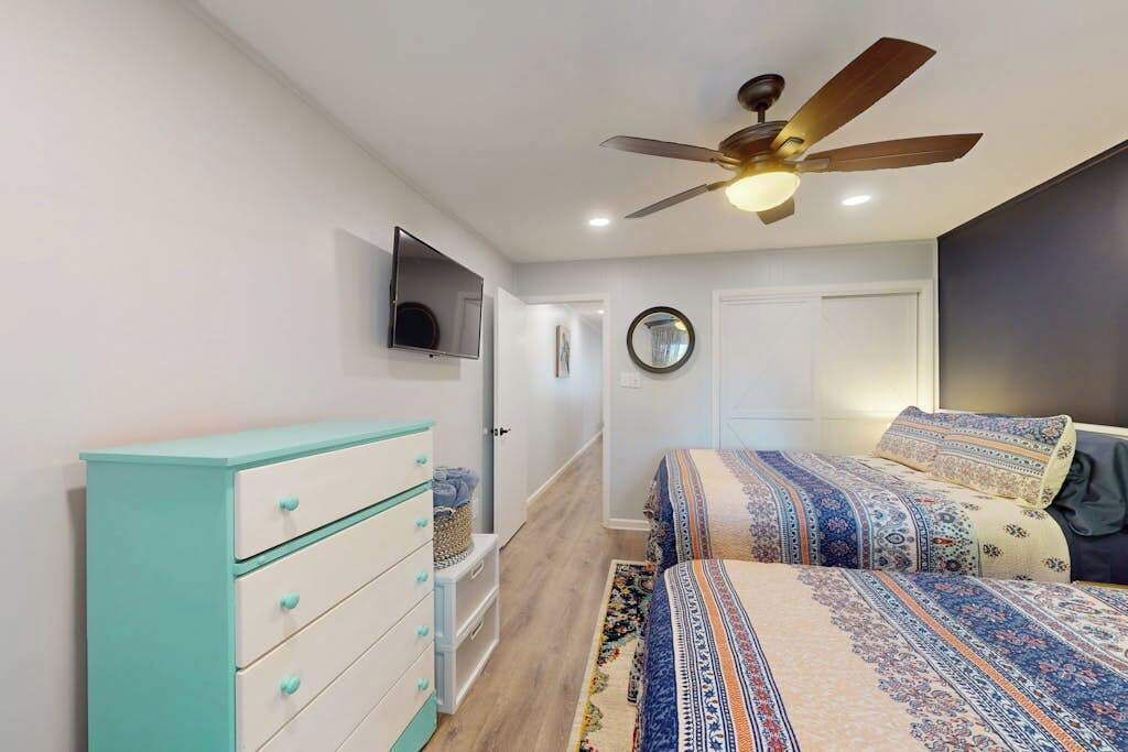 A bedroom with a bed, a ceiling fan, a TV, and a dresser.