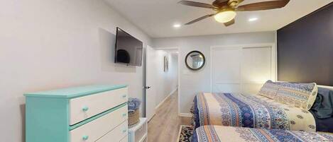 A bedroom with a bed, a ceiling fan, a TV, and a dresser.