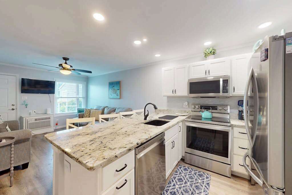 A modern kitchen with white cabinetry, a granite countertop, a built-in microwave, an oven, and a refrigerator.