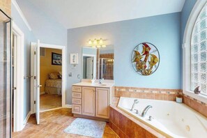 A bathroom with a large bathtub, a vanity with a mirror, and a decorative wall piece. - The Point 1437 (Ocean Pines)