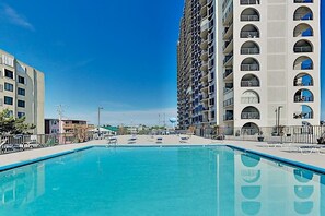 A swimming pool with lounge chairs, surrounded by high-rise buildings. - Sunny mid-town Condo w/water-views, beach access, pool, sundeck, & gym (Ocean City)