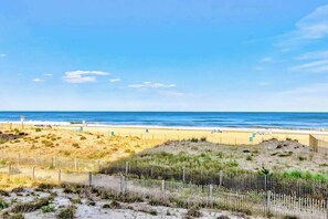 A beach with a wooden fence, sandy dunes, and the ocean in the background. - Sunny mid-town Condo w/water-views, beach access, pool, sundeck, & gym (Ocean City)