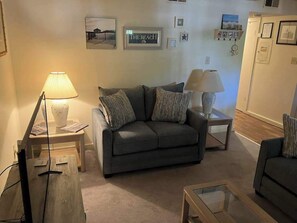 A living room with a sofa, two side tables with lamps, a glass coffee table, and a small table with a lamp. - Our Place At The Beach 202I (Ocean City)