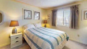 Una camera da letto con un letto, due lampade da comodino, un comodino, una finestra con tende e quadri appesi al muro.