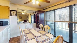 Zona pranzo con tavolo, sedie, ventilatore a soffitto e vista attraverso ampie finestre.
