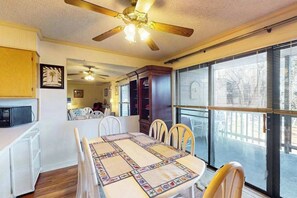A dining area with a table, chairs, a ceiling fan, and a view through large windows. - Our Place At The Beach 202I (Ocean City)