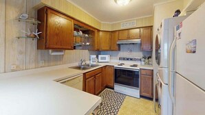 A kitchen with wooden cabinets, a microwave, an oven, and a refrigerator. - Midtown Ocean City Condo short walk to beach, restaurants & shops (Ocean City)