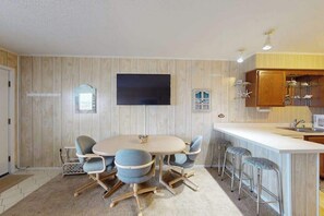 Una cocina moderna con una mesa redonda para comer, taburetes de bar y un televisor de pantalla plana montado en la pared.