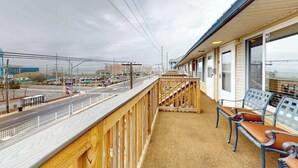 A balcony with a view of a street, a bench, and a building with large windows. - Midtown Ocean City Condo short walk to beach, restaurants & shops (Ocean City)