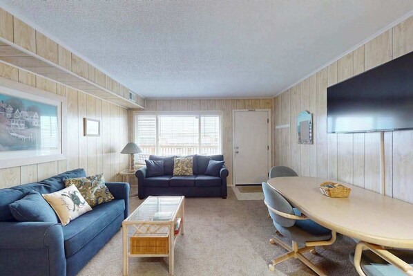 Una habitación con un sofá azul, una mesa de centro, una mesa de comedor y un televisor montado en la pared.