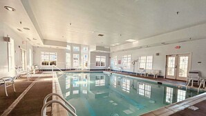 Ein großes Hallenbad mit klarem Wasser, umgeben von weißen Wänden und mehreren Fenstern.