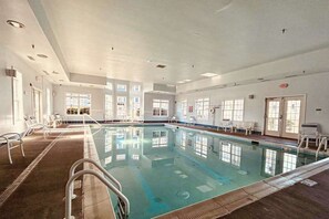 Ein großes Hallenbad mit klarem Wasser, umgeben von weißen Wänden und mehreren Fenstern.