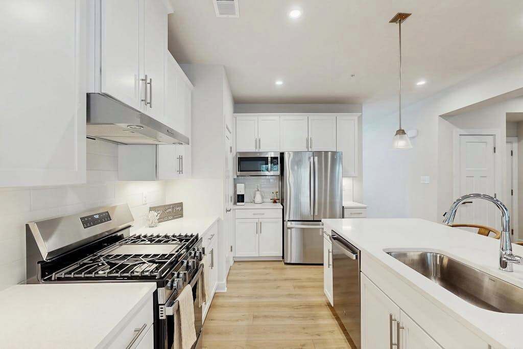 A modern kitchen with white cabinetry, stainless steel appliances, and a wooden floor.