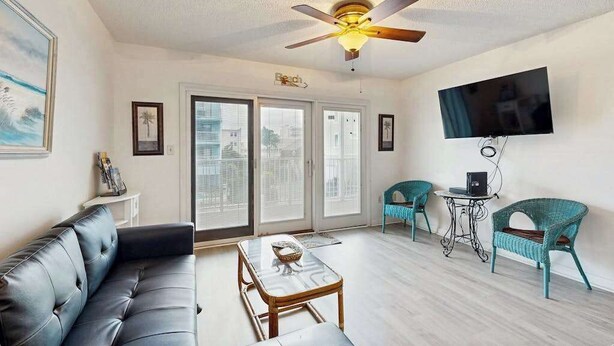 Un salon comprenant un canapé, une table basse, un ventilateur de plafond, un téléviseur et deux fauteuils.