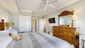 A bedroom with a large bed, a wooden dresser, a ceiling fan, and a television. - Astoria 302 (Ocean City)