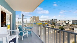 A balcony with a view of a street, a building with a sign, and a parked car. - Astoria 302 (Ocean City)